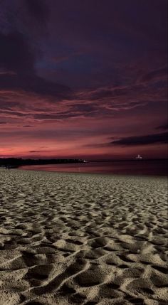 the sky is purple and red as the sun sets on the beach with waves in the sand