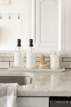 three bottles on a counter in front of a sink with soap dispensers