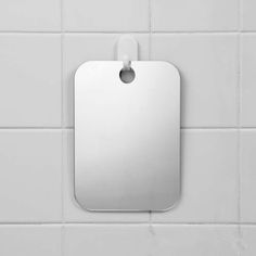 a white tile wall with a square metal tag hanging on it's left side