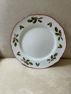 a white plate with holly and red trim on the edge is sitting on a couch