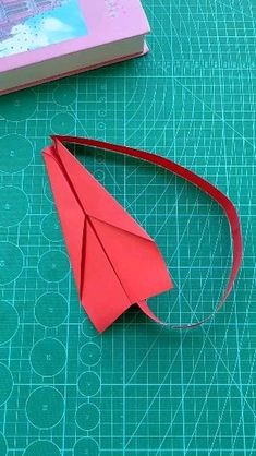 a red paper airplane sitting on top of a table next to a book and scissors