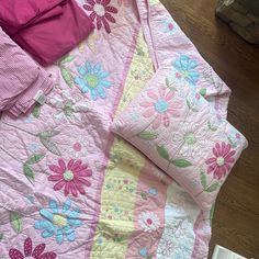 a child's bed with pink and blue quilts on the floor next to a book