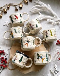 six coffee cups with designs on them sitting on a wooden tray next to christmas decorations