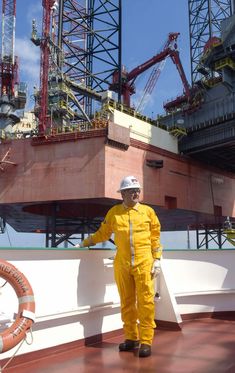 a man in yellow coveralls and hard hat standing on the deck of a ship