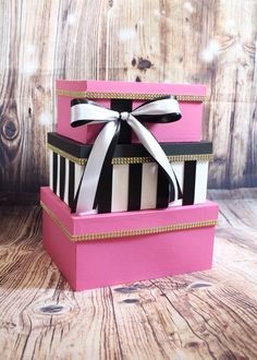 three pink boxes with black and white striped designs on them, one has a bow at the top