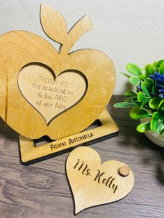 two wooden hearts with names on them sitting next to a potted plant and vase