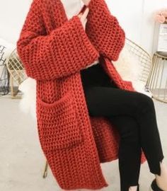 a woman sitting in a chair while holding a cell phone to her ear and wearing a red knitted cardigan