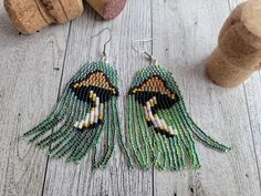 a pair of green and yellow beaded earrings on top of a wooden table next to corks