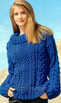 a woman wearing a blue sweater and black pants standing in front of the ocean with her hands on her hips