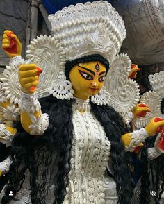 an elaborately dressed woman in white and black costume with yellow accents, holding up her hands