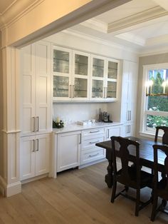 a dining room table and chairs in front of a window with white cabinets on either side