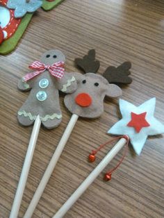 three felt christmas decorations on sticks sitting on a wooden table next to other crafting supplies