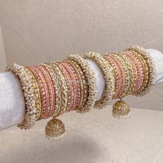 Large stack of luxurious Heavy Pearl & Antique Gold bangles with a mix of Pink shades finished with jhumka drops and zircon crystals. The perfect stack for any Bride or those wanting to make a statement. Ready to Ship as pictured. Bridal Bangle Set Indian, Bridal Jewelry Sets Brides, Thread Bangles Design, Indian Bridal Jewelry Sets, Jewelry Set Design, Glass Bangles, Indian Jewellery Design Earrings