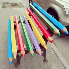 there are many colored pencils sitting on the back of a bench in front of a car