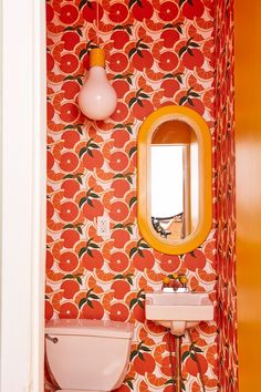 a bathroom with orange and white wallpaper has a yellow mirror above the toilet bowl