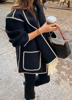 a woman standing on the sidewalk holding a cup of coffee