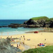 people are on the beach and in the water near some rocks, sand and grass