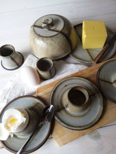 a table topped with plates and cups filled with food on top of a wooden cutting board