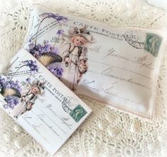 two envelopes are laying on top of a lace doily, one has a teddy bear and the other has flowers