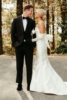 a bride and groom standing in the middle of an empty road with trees behind them