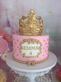 a pink and gold birthday cake with a crown on top is sitting on a table