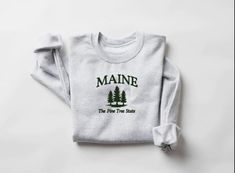 Experience the cozy comfort of our embroidered Maine sweatshirt, a perfect blend of style and warmth that showcases your love for the Pine Tree State. This high-quality sweatshirt features a beautifully crafted design that highlights Maine's natural beauty, making it an ideal choice for both casual outings and relaxing afternoons at home. Made from soft, durable fabric, it ensures you stay comfortable while adding a touch of Maine charm to your wardrobe. Whether you're exploring the great outdoors or simply enjoying a leisurely day, this sweatshirt is a must-have for anyone who appreciates the unique spirit of Maine. Grab yours today and celebrate the beauty of the Pine Tree State! Maine Sweatshirt, Alabama Sweatshirt, State Crewneck, Forks Washington, Maine State, State Of Maine, Embroidered Sweatshirts, Pine Tree, Comforters Cozy