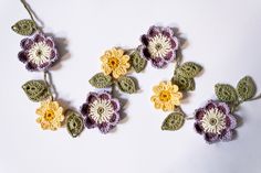 crocheted flowers are arranged on a white surface with green leaves and yellow centers