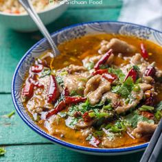 a bowl filled with meat and vegetables on top of a wooden table next to rice