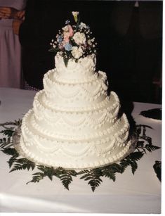 a white wedding cake sitting on top of a table covered in flowers and greenery