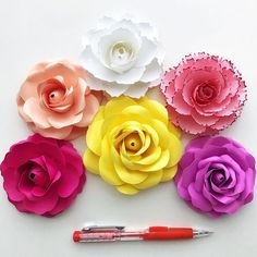 several paper flowers and a pen on a white surface with one flower in the middle