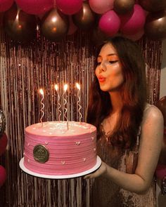 a woman standing in front of a pink cake with candles on it and balloons behind her