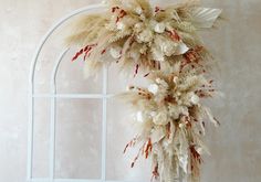 a white arch decorated with dried flowers and feathers in front of a beige stucco wall