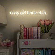 a book shelf with books and flowers on it next to a lamp that reads cosy girl book club