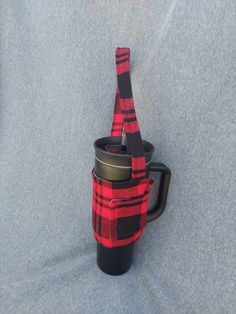 a red and black plaid coffee cup holder on a gray surface with a metal mug in it