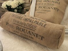 two burlap pillows sitting on top of a bed next to a vase with white flowers