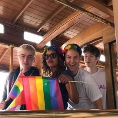 a group of young people standing next to each other in front of a mirror holding a rainbow flag