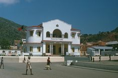 people are walking around in front of a large white building with red trim and windows