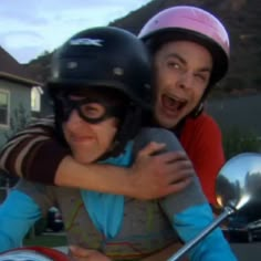 a man and woman riding on the back of a motor scooter with their arms around each other