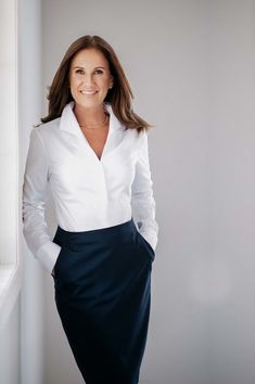 a woman in a white shirt and black skirt posing for the camera with her hands on her hips