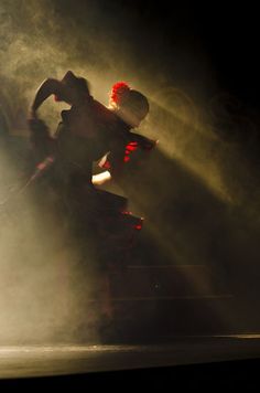 two people are dancing in the dark on stage with light coming from behind their backs