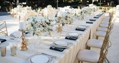 a long table is set with white flowers and place settings for an elegant dinner party