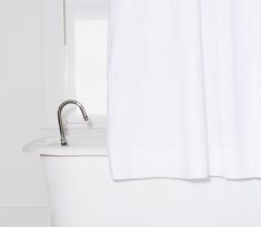 a white bath tub sitting next to a window with a curtain on it's side