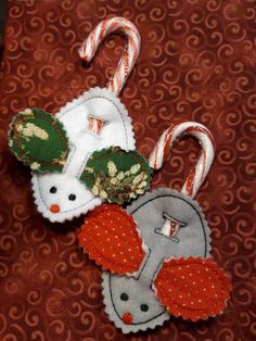 two christmas ornaments are sitting on a red table cloth with candy canes in the background