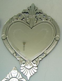 an ornate heart shaped mirror on the wall next to a candle holder and two mirrors