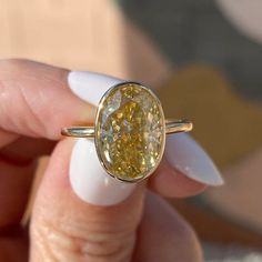 a close up of a person holding a ring with an oval shaped yellow diamond in it