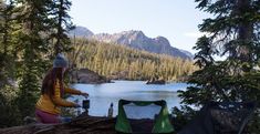 a woman sitting on top of a log next to a lake