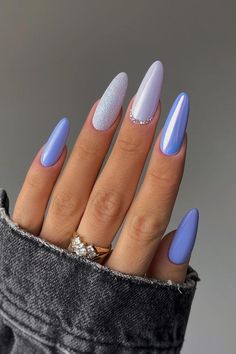 Elevate your style with these almond-shaped purple nails, showcasing a variety of dreamy designs. The pastel purple base is complemented by a sugar glitter finish on one and adorned with a subtle rhinestone crescent on another. The remaining nails are graced with a smooth, iridescent sheen, creating a harmonious yet captivating look. Perfect for adding a touch of elegance to any outfit. ✨  // Photo Credit: Instagram @pegi_nails Nail Inpos Ideas Almond, Icy Blue Nail Designs, Iridescent Purple Nails, Summer Nails Oval Shape, Pretty Nails Almond, Birthday Nails Purple, Trendy Purple Nails, Purple Summer Nails, Periwinkle Nails