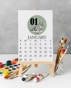 an easel with paint and brushes on it next to a calendar that says january