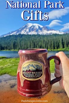 a person holding a coffee mug with the words national park gifts in front of a mountain