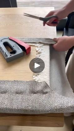 someone is cutting fabric with scissors on a wooden table in the process of making a chair cushion